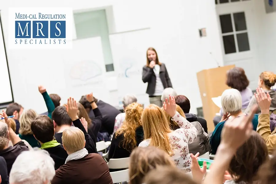 Audience members raising hands at a Medi-Cal seminar in California, led by a speaker providing expert guidance on eligibility, application processes, and healthcare benefits.