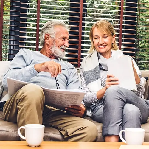 Smiling senior couple relaxing with coffee and documents representing Medi-Cal Regulation Specialists assisting with HCBS Waiver Program planning and support